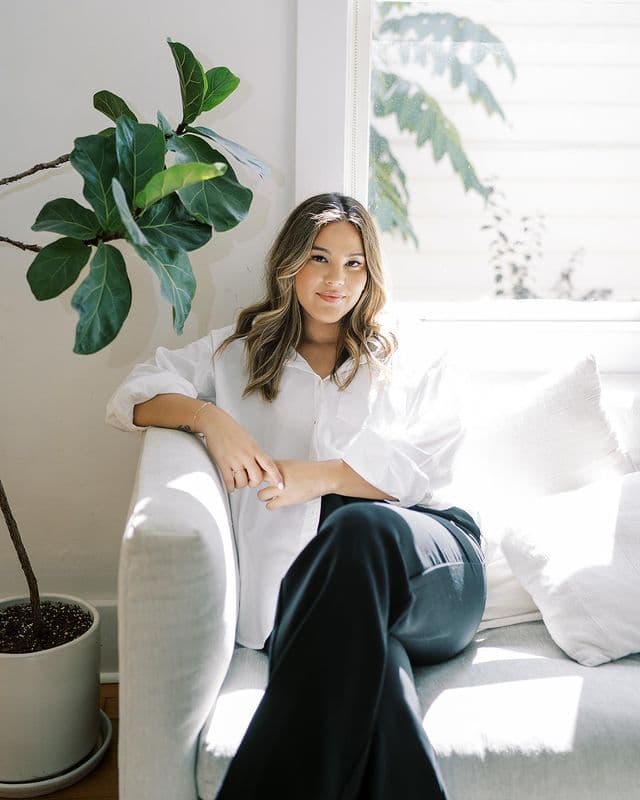 Modimal model in a white shirt and dark trousers seated by a window